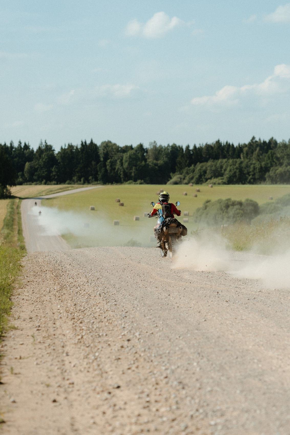 Enduro motociklininkas dulkėtame žvyrkelyje tarp laukų