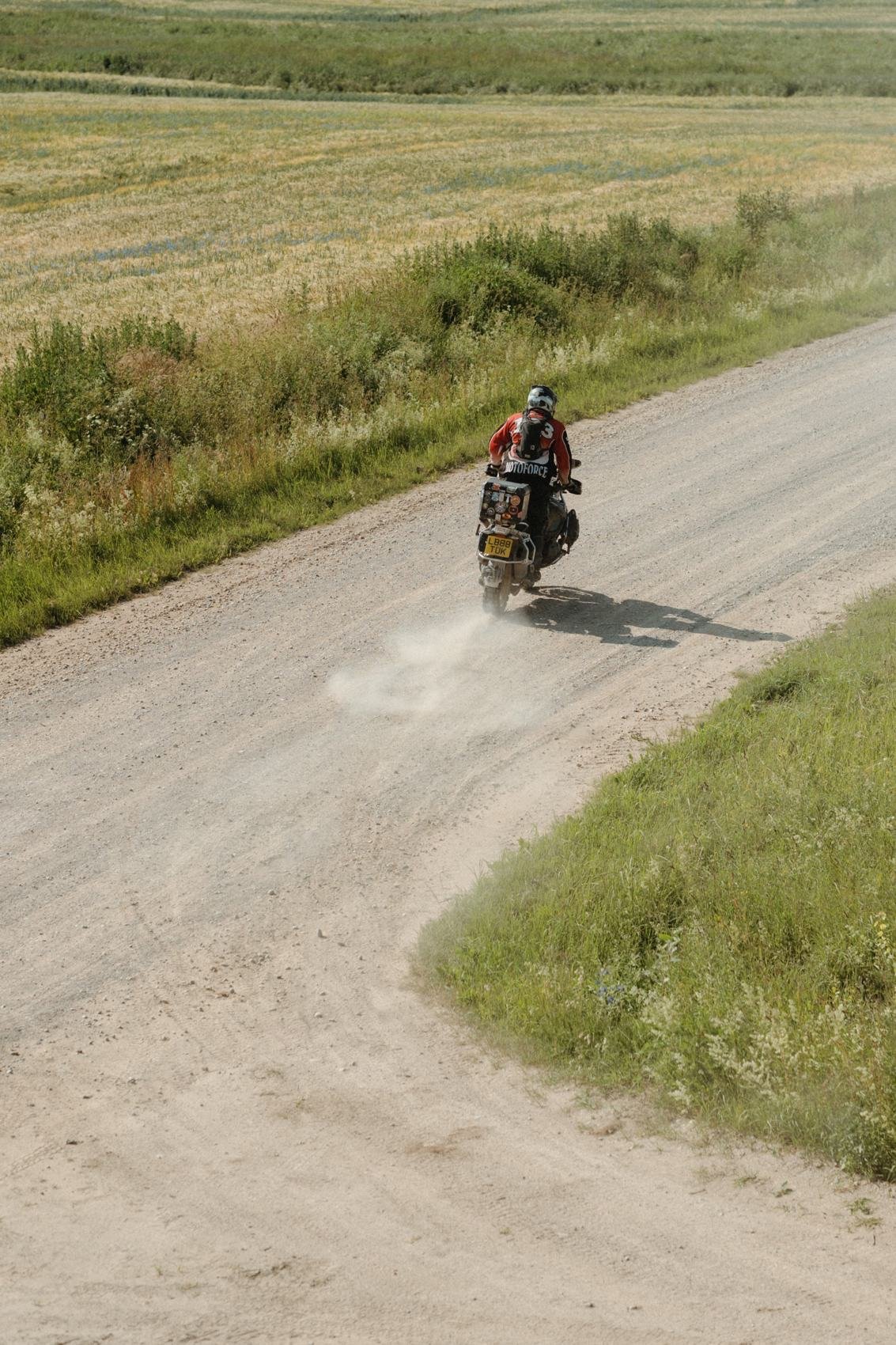 Motociklininkas vingiuotame žvyrkelyje tarp laukų